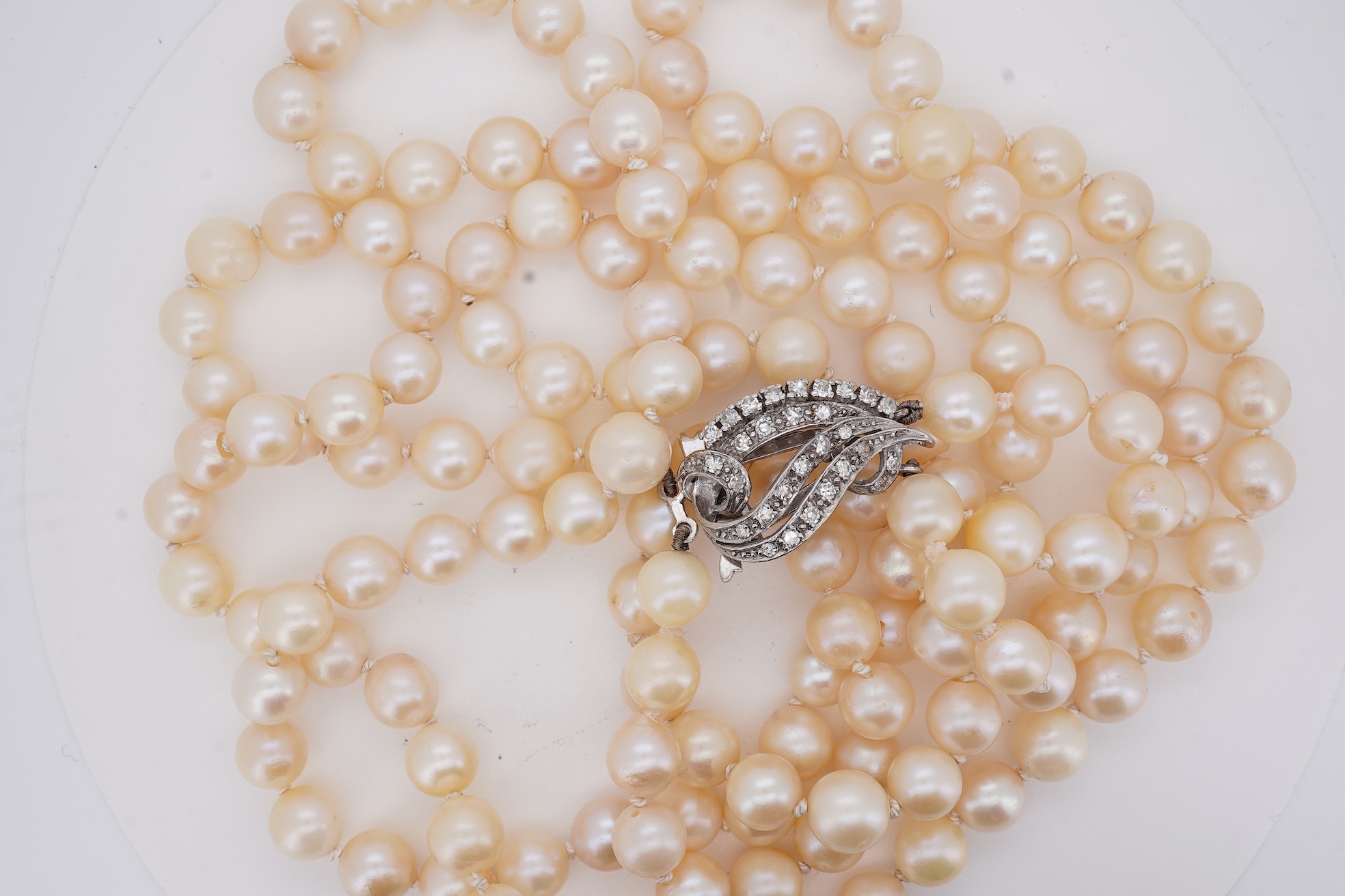 A twin strand cultured pearl necklace with a diamond cluster set white metal scroll shaped clasp, 60cm.
